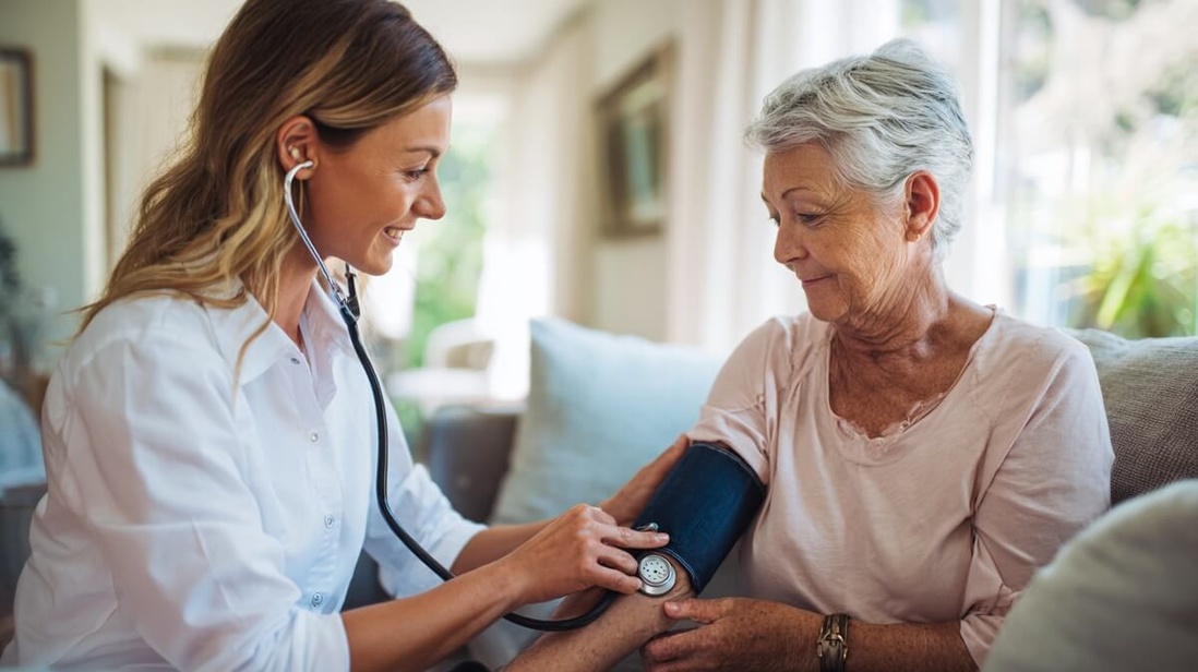 Une infirmière libérale effectue une consultation à domicile auprès d'une patiente senior dans un intérieur lumineux © SeniorActu