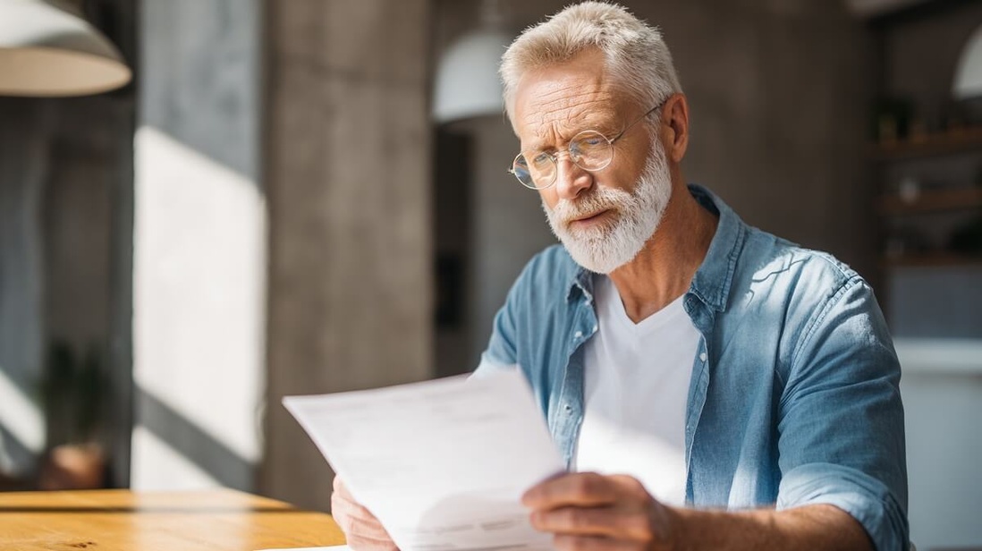 Un homme senior examine attentivement sa facture d'électricité © SeniorActu