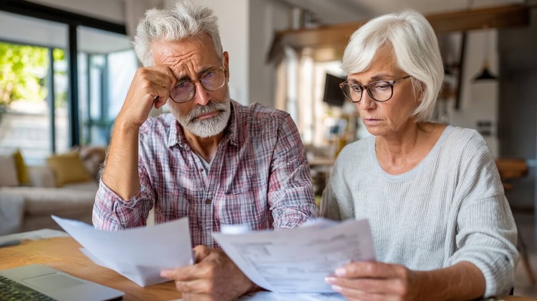 Un couple senior un peu dépité examine des documents d'épargne retraite © SeniorActu