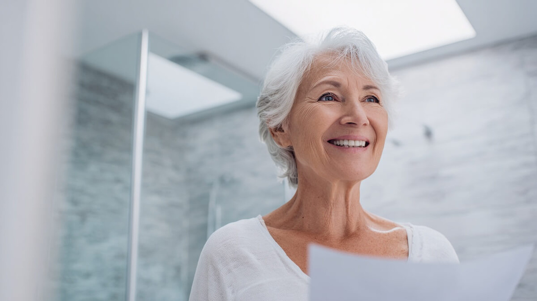Une femme senior examine un devis de travaux d'adaptation dans sa salle de bain © SeniorActu