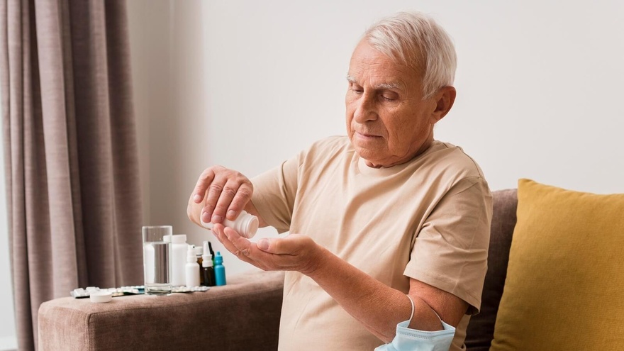 Un senior verse des comprimés dans sa main, assis sur son canapé © Freepik - Magnific.com