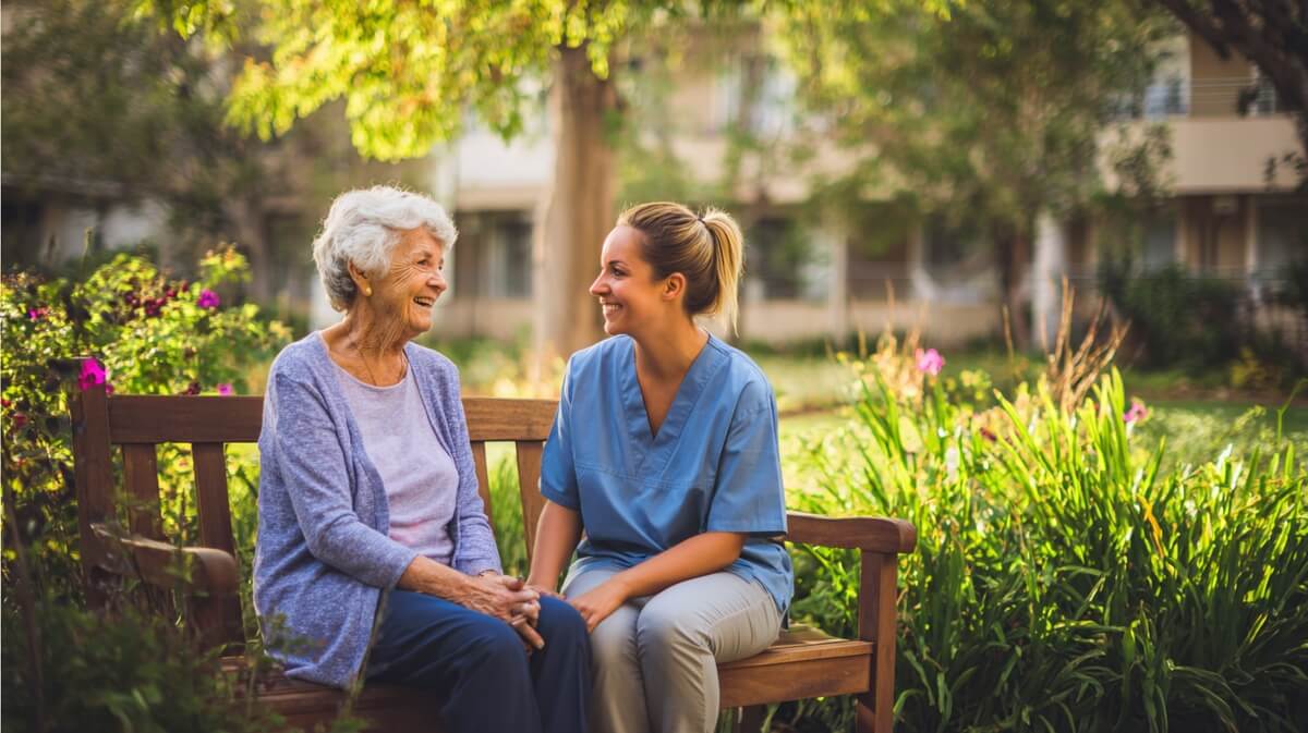 Résidente âgée sur un banc dans le jardin d'un EHPAD, en compagnie d'une aide-soignante © SeniorActu